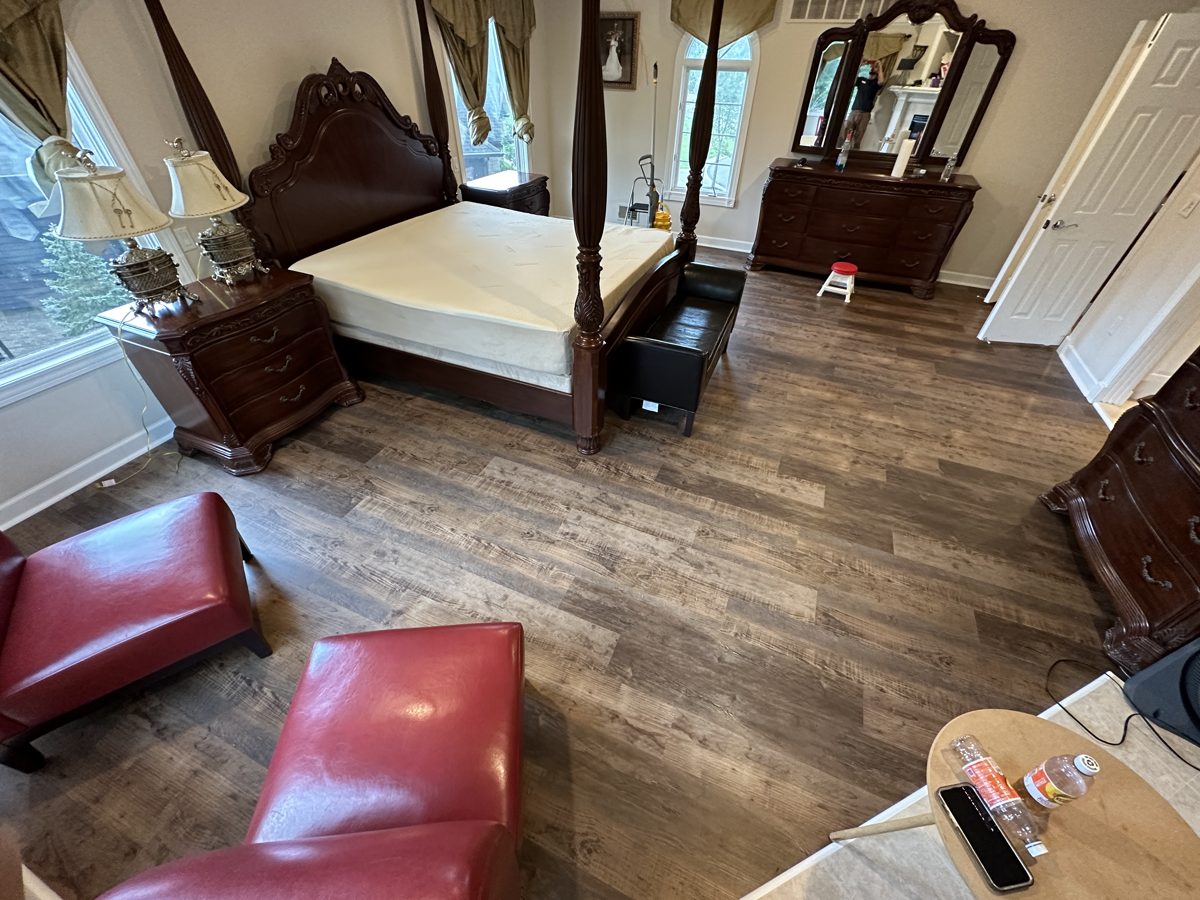 Large bedroom with mid-brown, rustic wood-look plank flooring
