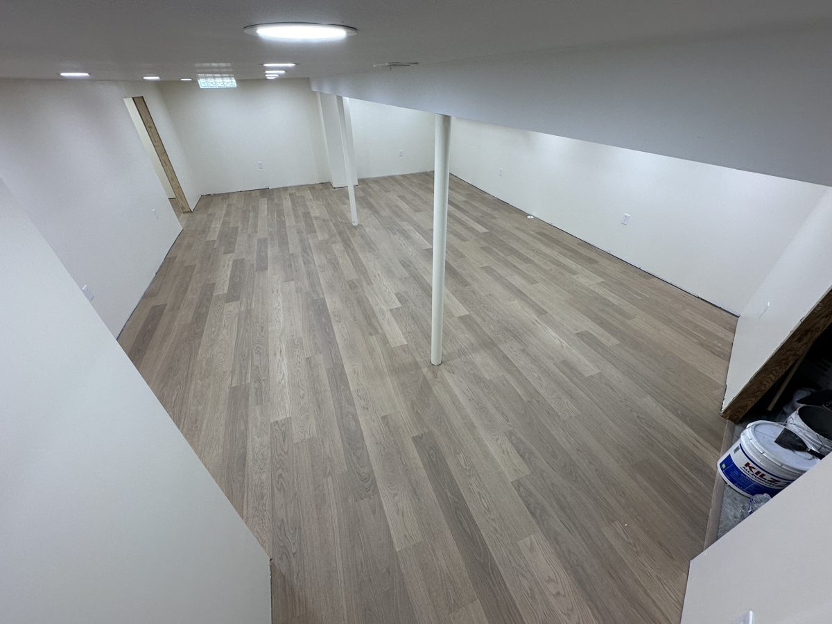 Finished basement with light grey-brown plank flooring and white support posts